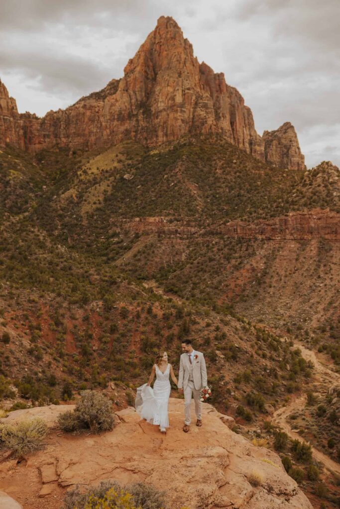 A bride and groom walking hand in hand with Zion behind them