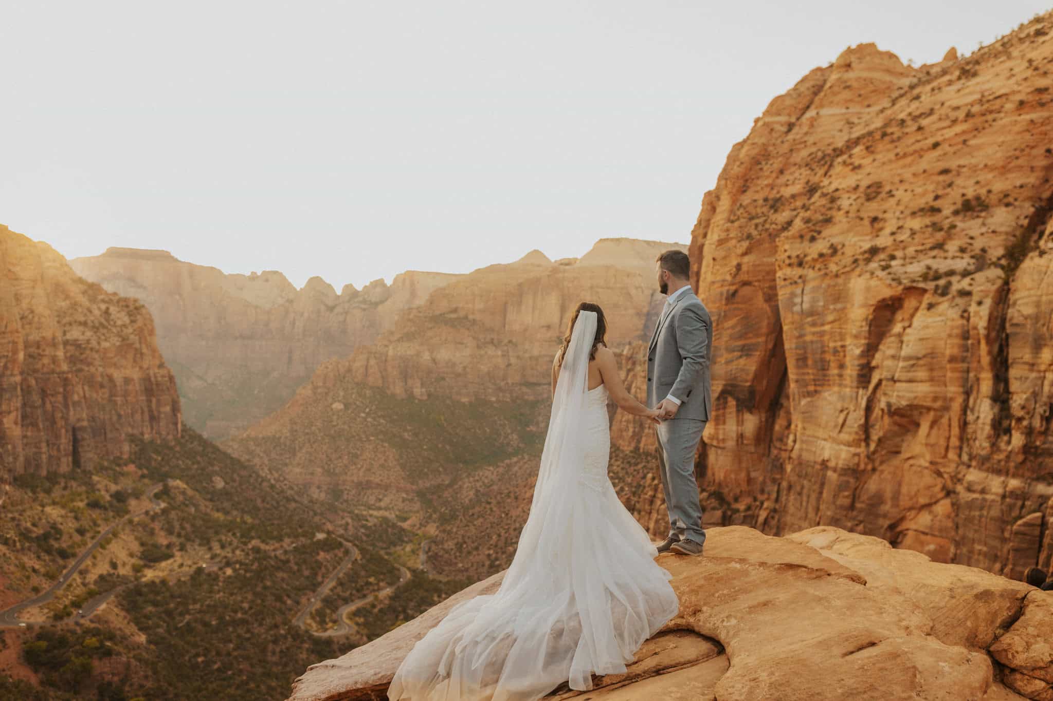 An elopement couple standing on a ledge over looking Zion Canyon Overlook
