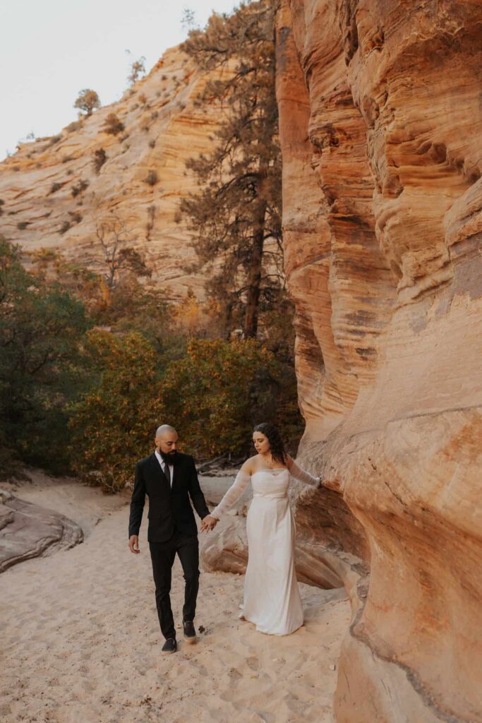 A bride and groom holding hands walking through a fall foliage slot canyon in Zion during the fall season.