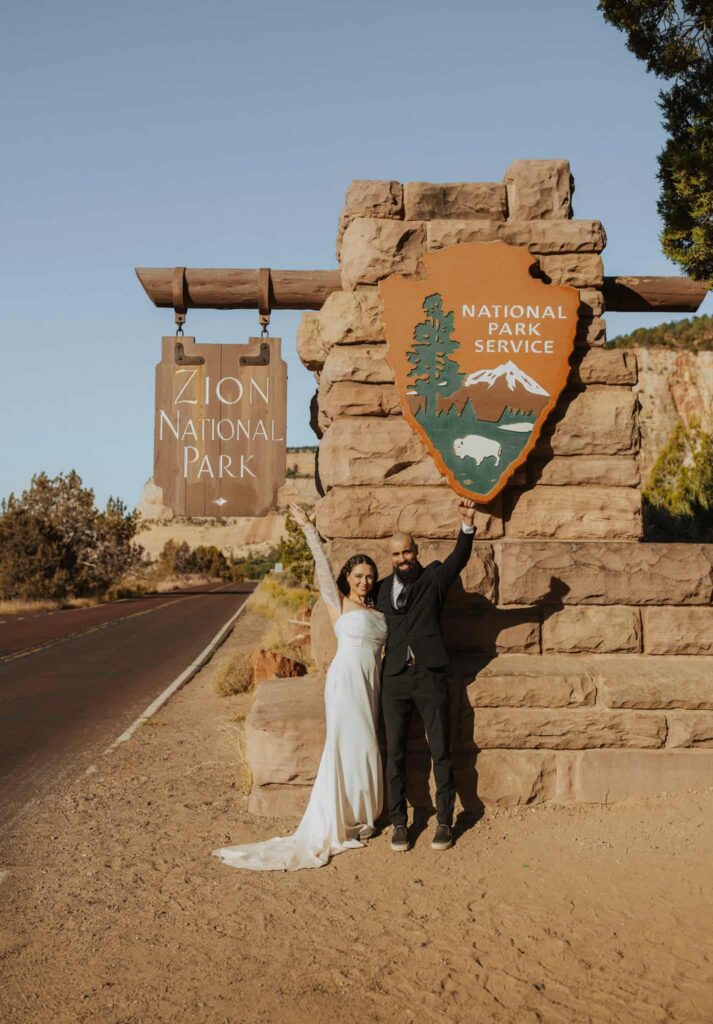 A couple cheering next to the Zion National Park entrance sign