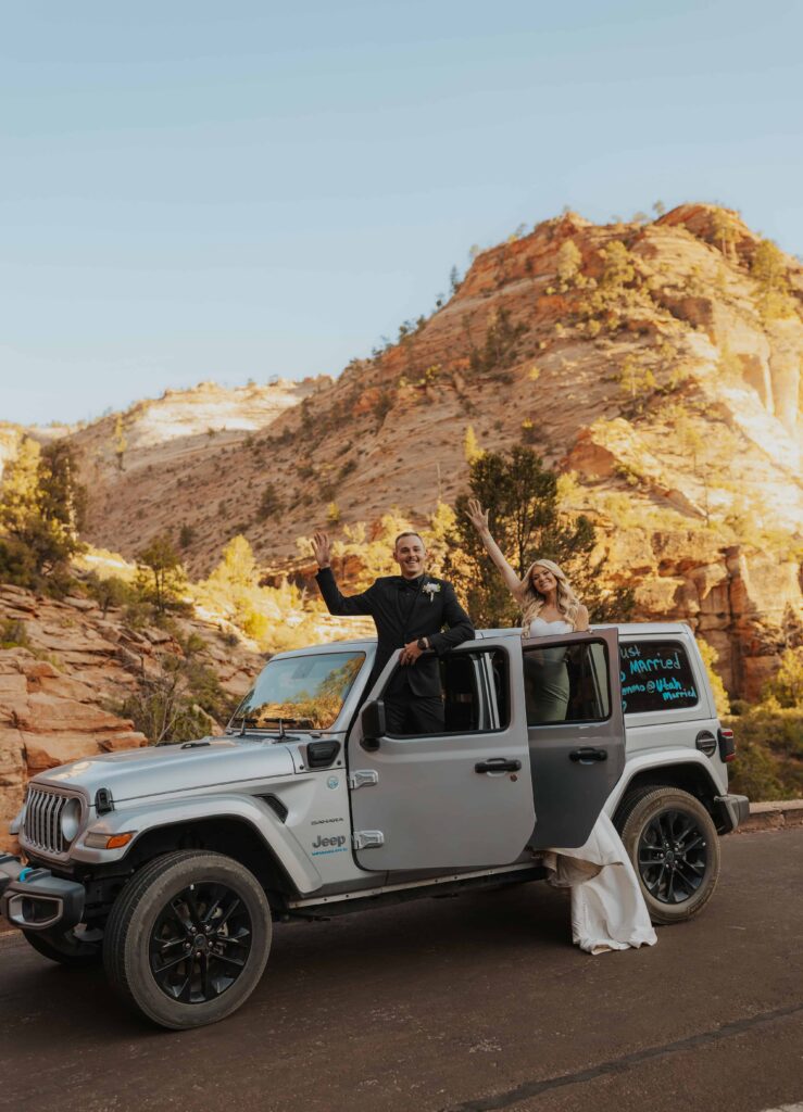 A bride and groom waving as they hang out of a Jeep in Zion during the summer time.