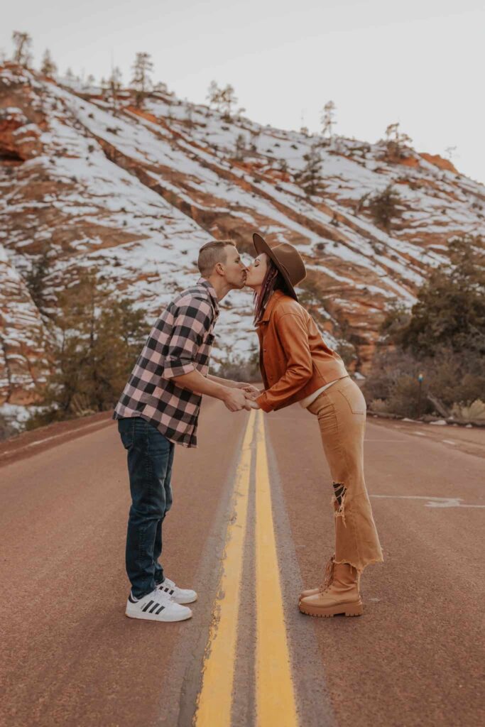 A couple kissing in the middle of a snowy backdrop in Zion during the wintertime. 