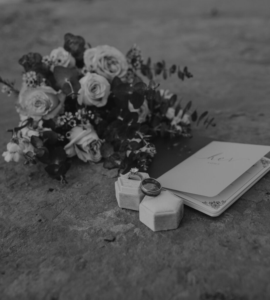 a black and white photo of florals, wedding rings, and a vow book in Zion.