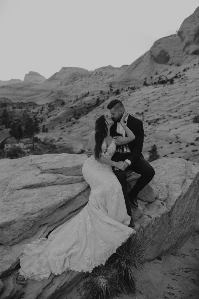 An elopement couple sharing a kiss while sitting on a ledge in Zion National Park. 