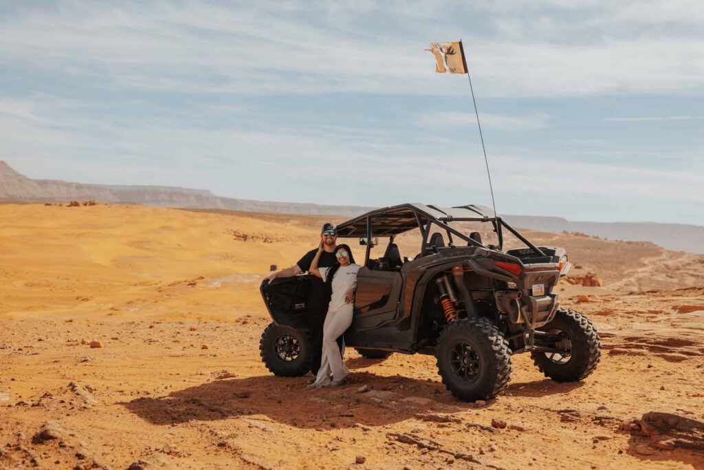 A couple posing next to their UTV on their wedding day in the Sand Dunes. 