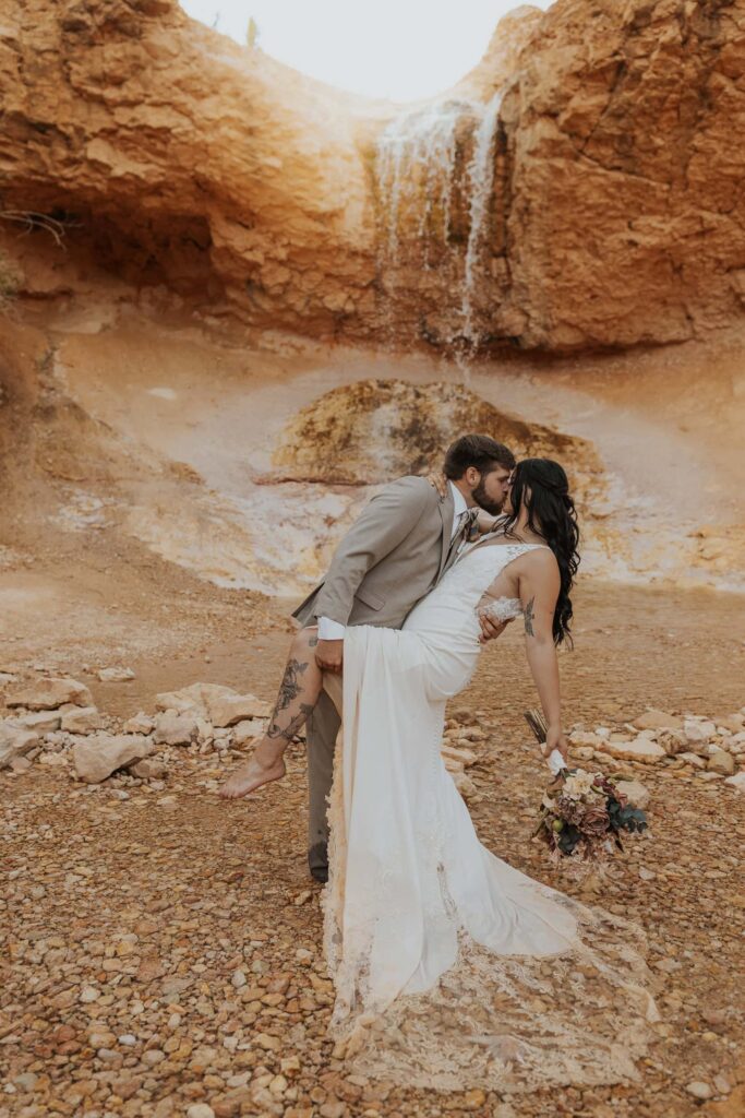 A bride and groom kissing in front of a waterfall.