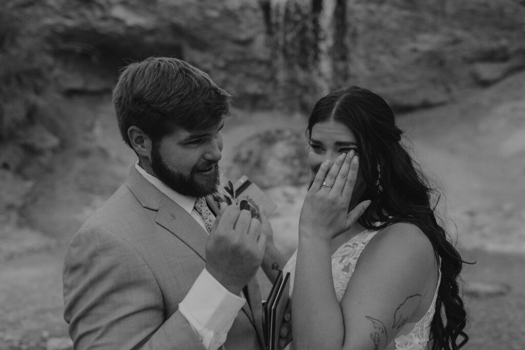 An emotional moment for a bride and groom wiping away tears after reading vows near a waterfall