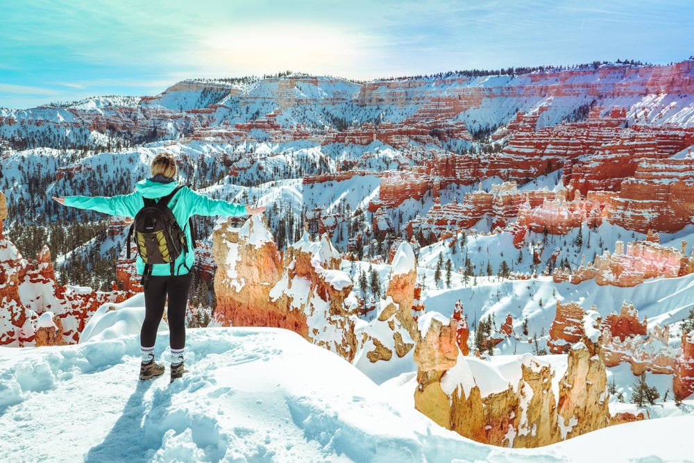 Bryce Canyon in the winter. With a hiker standing in front of the snow on the orange hoodoos.